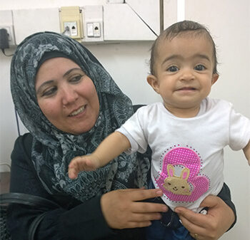 A smiling mother with her child visits Al Ahli Hospital in Gaza.  © ABM/Julianne Stewart, 2017