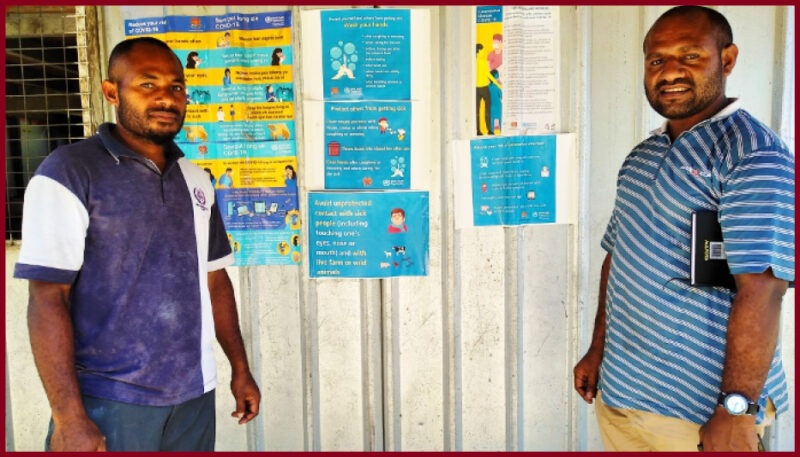 Head Teacher Mr Elizah Daka (L) shows CPP Monitoring and Evaluation Officer, Mr Bonnie Mombo, the COVID-19-related educational materials posted at the entrance to his school. © Bonnie Mombo, PNG Church Partnership Program, 2020.